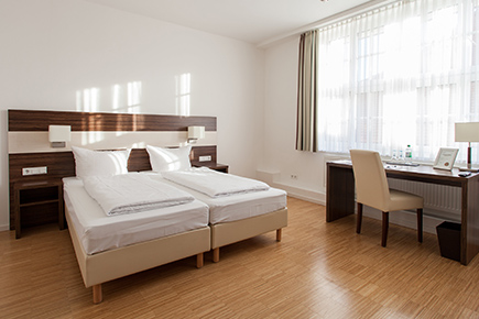 Bett eines Doppelzimmers des Halben Mondes, rechts dunkelbrauner Schreibtisch am Fenster 