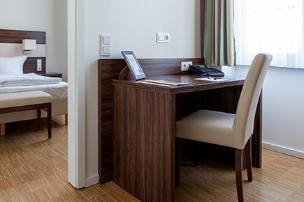 Blick auf Schlafzimmer aus dem Nebenraum mit Schreibtisch in einem der Hotelzimmer des Halben Mondes