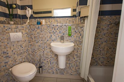 Blick in Badezimmer eines Hotelzimmers des Halben Mondes, links Toilette, mittig Waschbecken, rechts Dusche